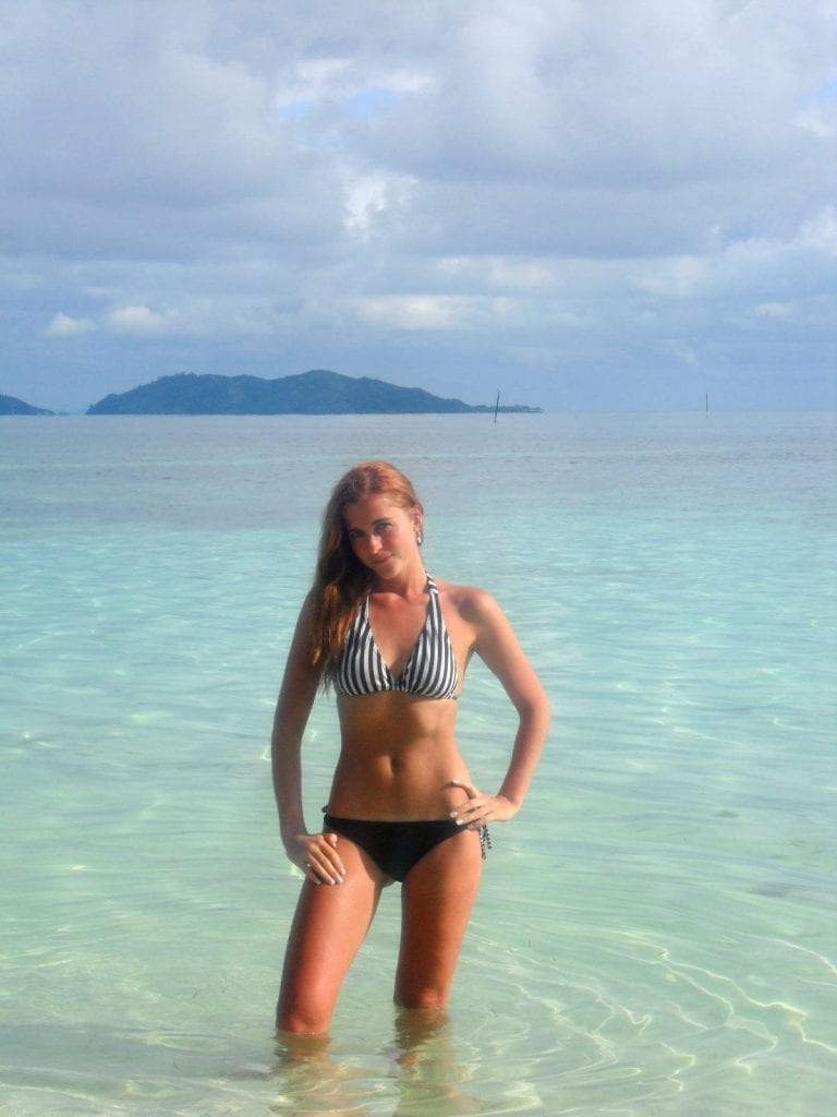 Women posing in front of blue water with mountain in distant background in Fiji