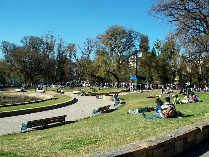 Busy public park with people relaxing and a clear blue sky, perfect for an outdoor Spanish language lesson.