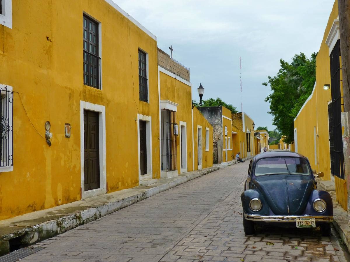 Classic scene of an old Volkswagen Beetle on a cobbled street with colonial buildings in vibrant yellow, a unique sight in Mexico's rich cityscape.
