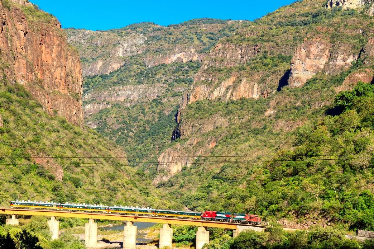Train crossing a bridge in a vast canyon, a stunning example of Mexico's unique landscapes and engineering marvels.

