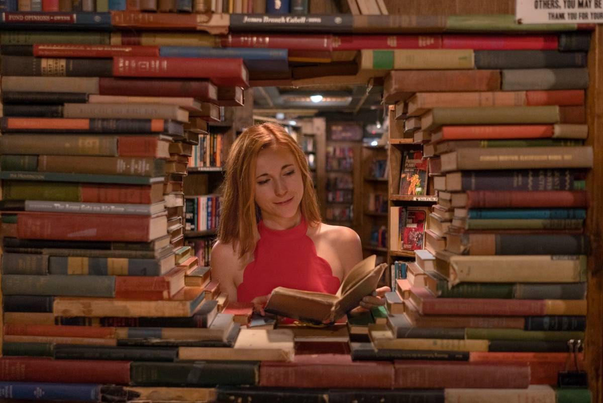 how to learn Spanish fast Woman reading a Spanish book in a cozy bookstore surrounded by towering stacks of books, immersing herself in the language.
