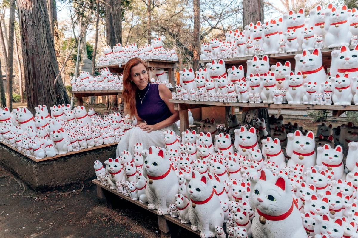 Woman surrounded by maneki-neko, or lucky cat figurines, in Tokyo's Gotokuji Temple.