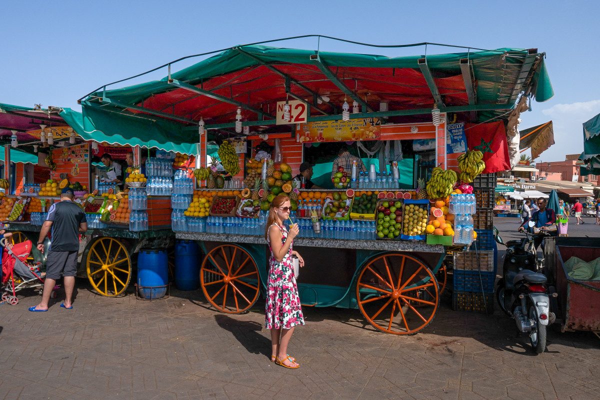 Marrakech Travel Tips Marrakesh A traveler enjoying a fresh fruit juice from a vibrant market stall in Marrakech, a refreshing tip for any Marrakech travel guide.