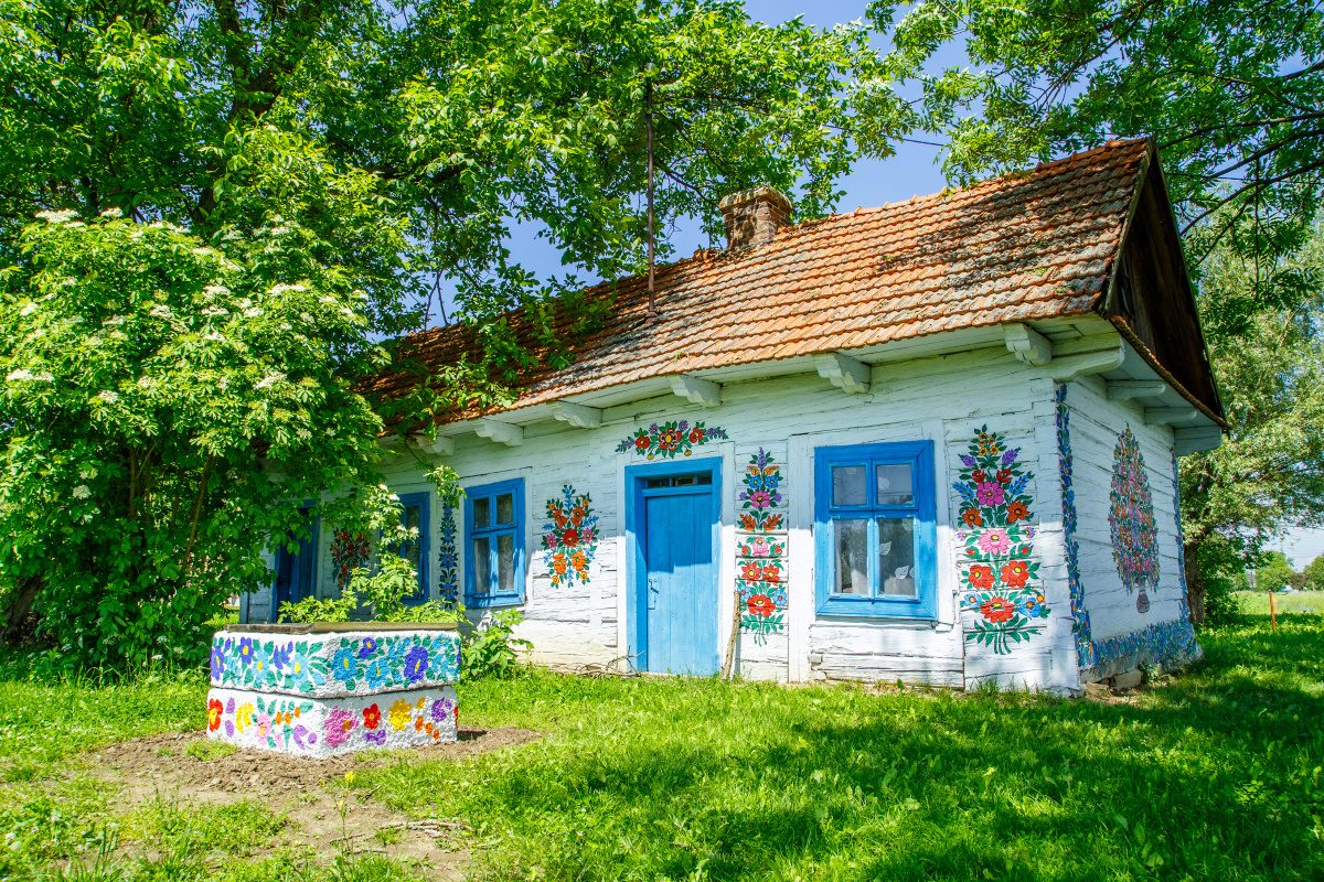 Zalipie Village A quaint and colorful Zalipie-style painted cottage in rural Poland, adorned with traditional floral folk motifs against lush greenery.
