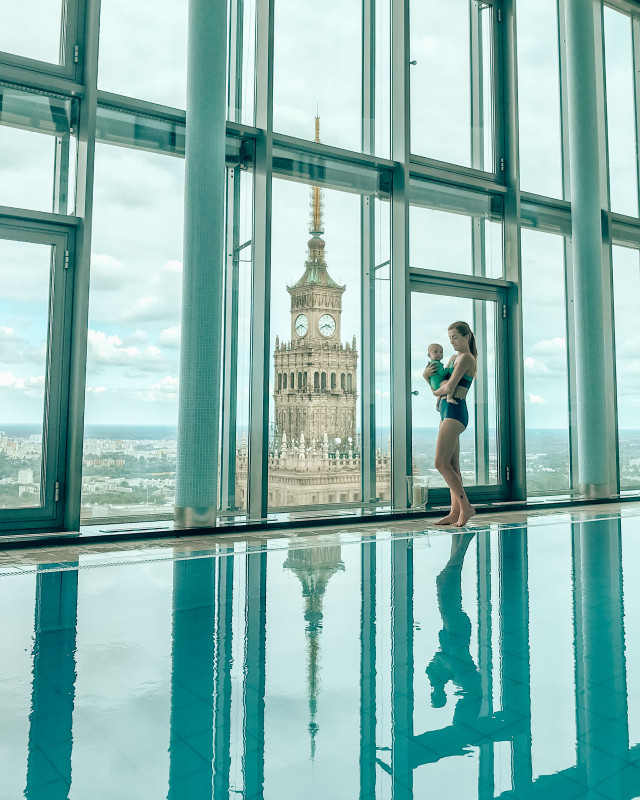 Woman with a baby overlooking Warsaw from a building with an indoor pool, a modern residential amenity for those living in Poland.