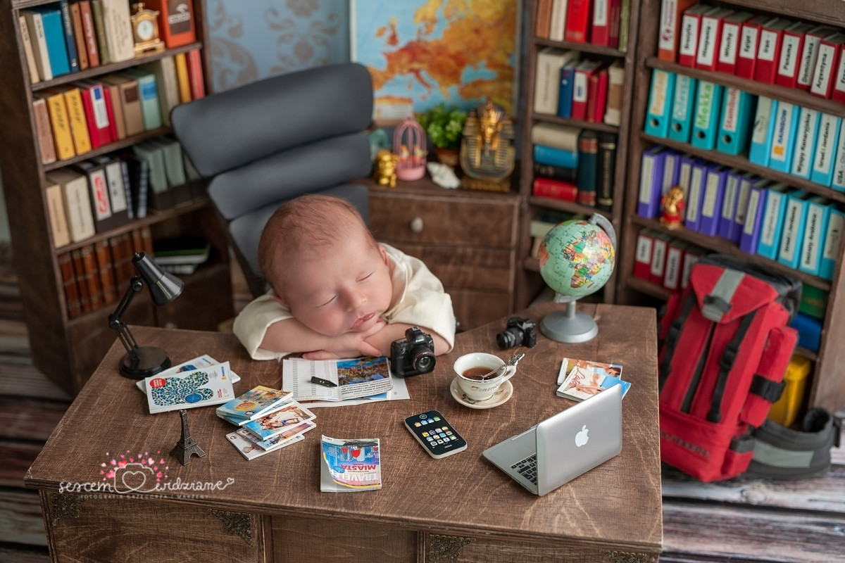baby traveler Baby dressed as a businessman at a desk covered with travel items and a laptop, humorously suggesting starting Spanish young.