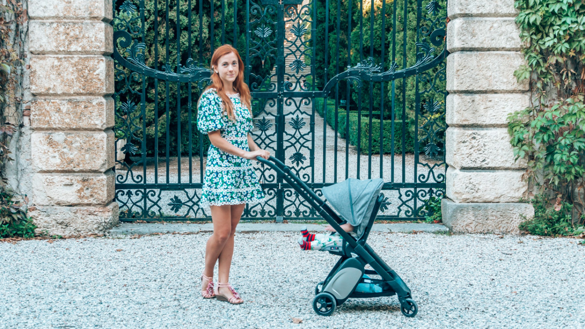 Woman with a travel stroller standing by an ornate gate, combining elegance with practicality for stylish parents on the go.