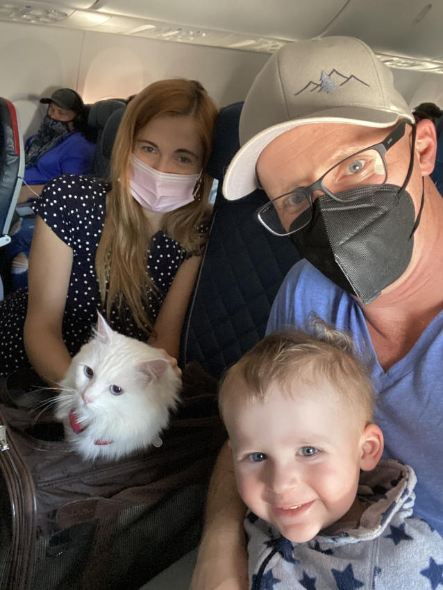 Family selfie on an airplane, with a toddler and a fluffy white cat, showing how to keep a 1-year-old entertained on a flight