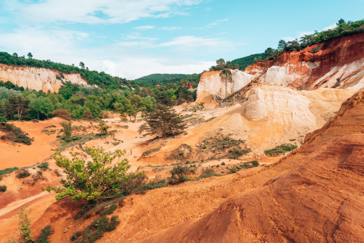 The ochre landscape of Roussillon offering a striking contrast with the lush greenery, a scenic drive destination in the French countryside that you can take if you decide to rent a car in France. Colorado Provencal