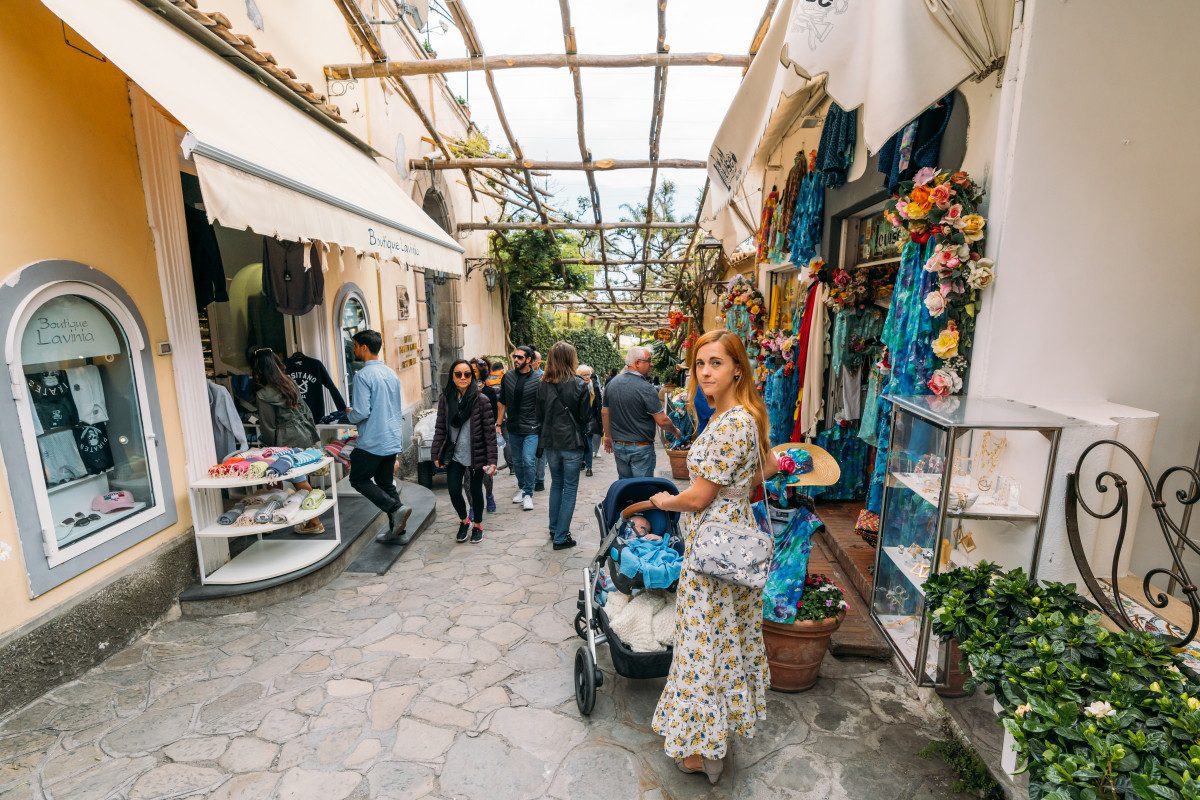 Mother pushing a stroller in a vibrant shopping alley, a perfect setting to explore what to buy in Italy.
