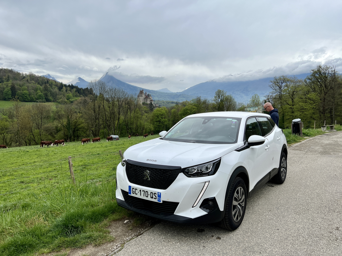 Crossing Borders from France to Monaco Car parked on a rural road with a backdrop of the French Alps and a castle, illustrating the picturesque drives awaiting when you rent a car in France.