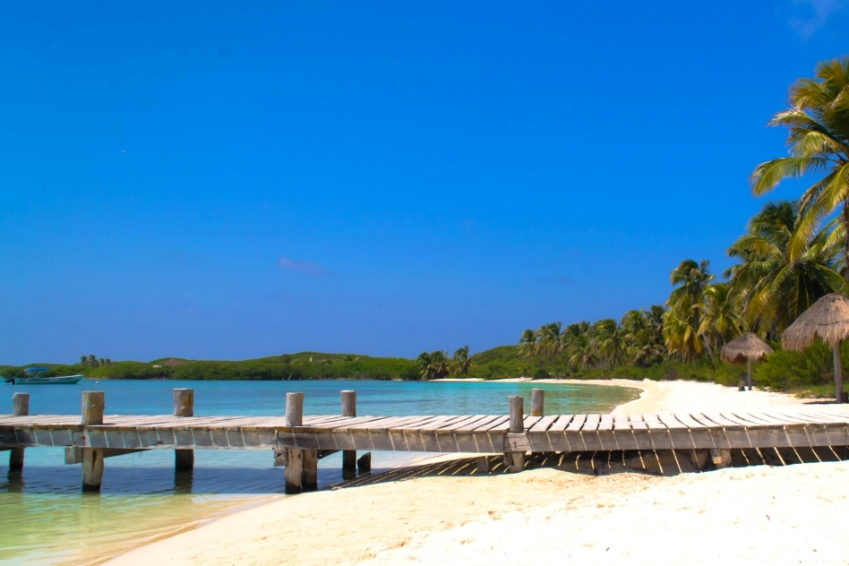 Wooden pier stretches into tranquil turquoise waters bordered by white sands and tropical greenery, an idyllic escape to one of Mexico's unique beaches.
