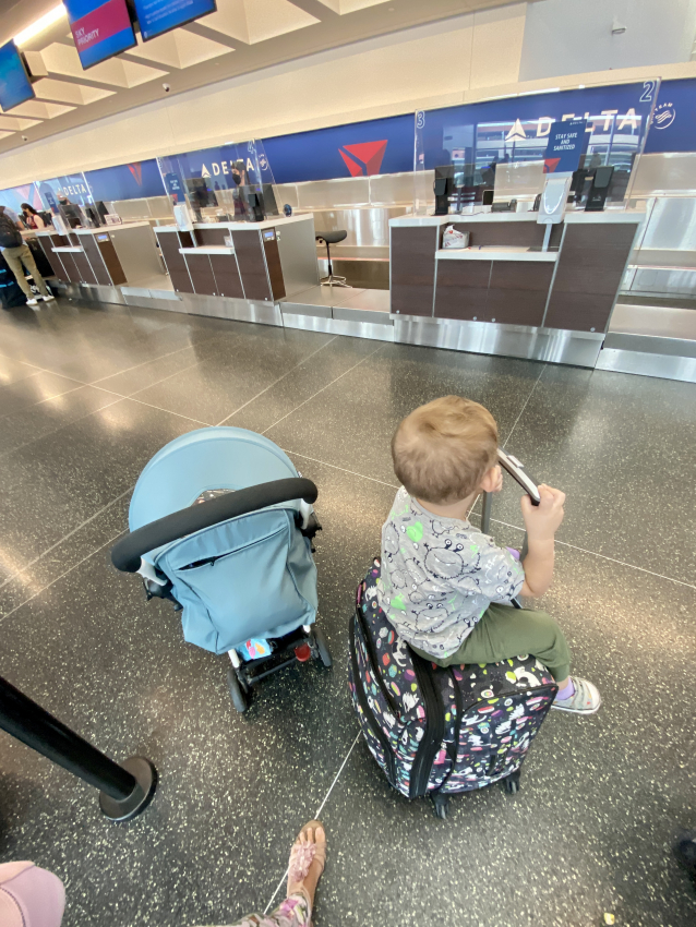 Toddler riding on luggage at the airport check-in area, a playful way to keep them entertained when flying with a toddler.