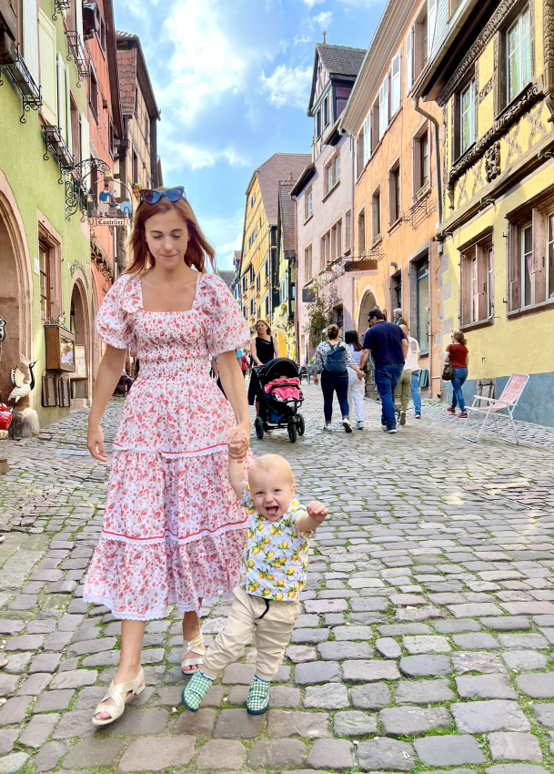 A toddler on a cobblestone street while walking with his mother in a colorful dress, capturing the essence of exploring France with baby.
