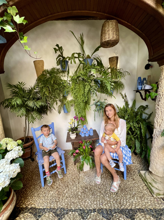 Cozy and lush indoor garden with a mother sitting with her baby and toddler, enjoying the tranquility of a green space in Spain.